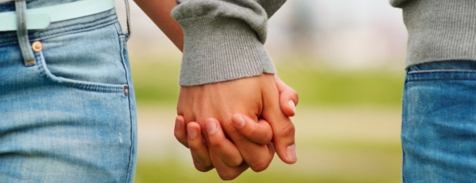 Mid section closeup image of a young couple holding hands, outdoors